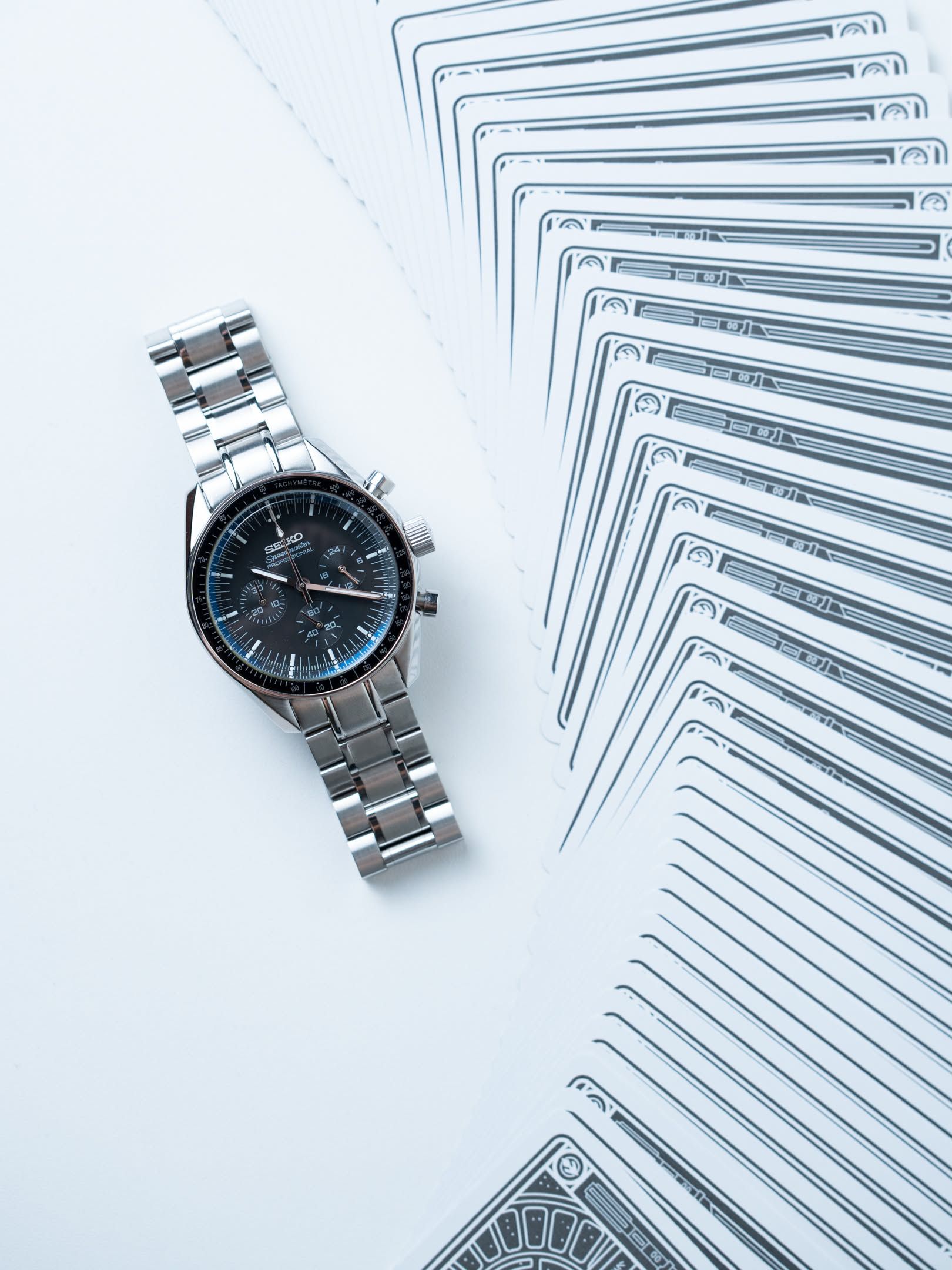 Ironwood lying flat beside a fanned deck of cards, the black dial and steel bracelet from above.