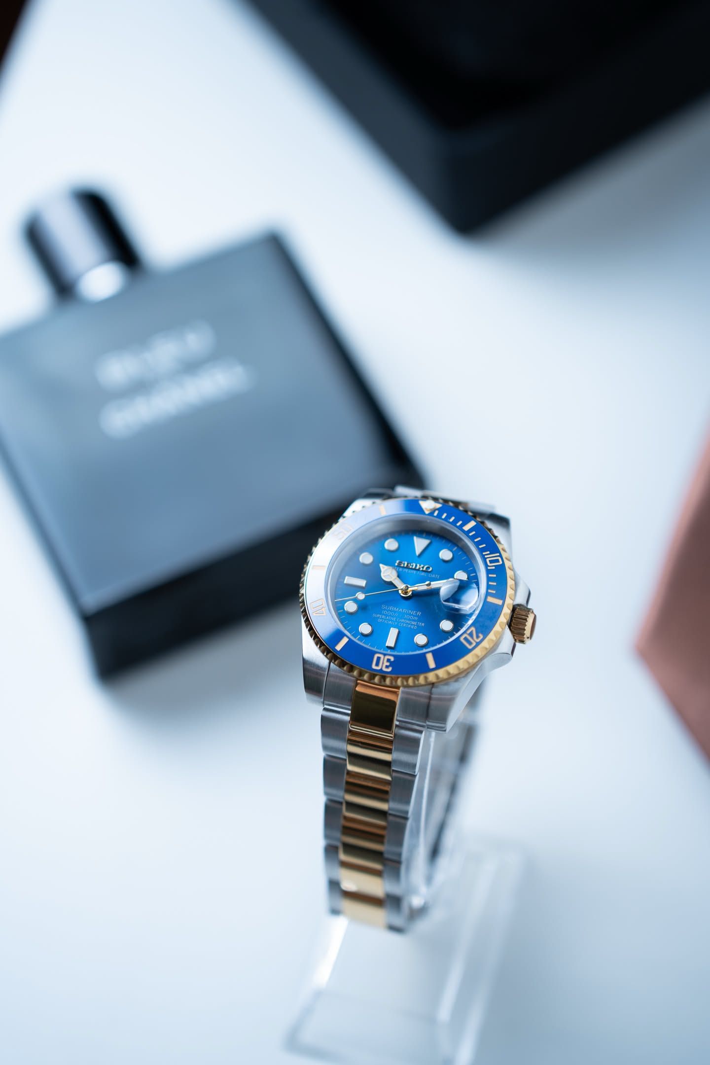 Bluegum on a clear stand, the blue bezel and gold crown turned toward the light.