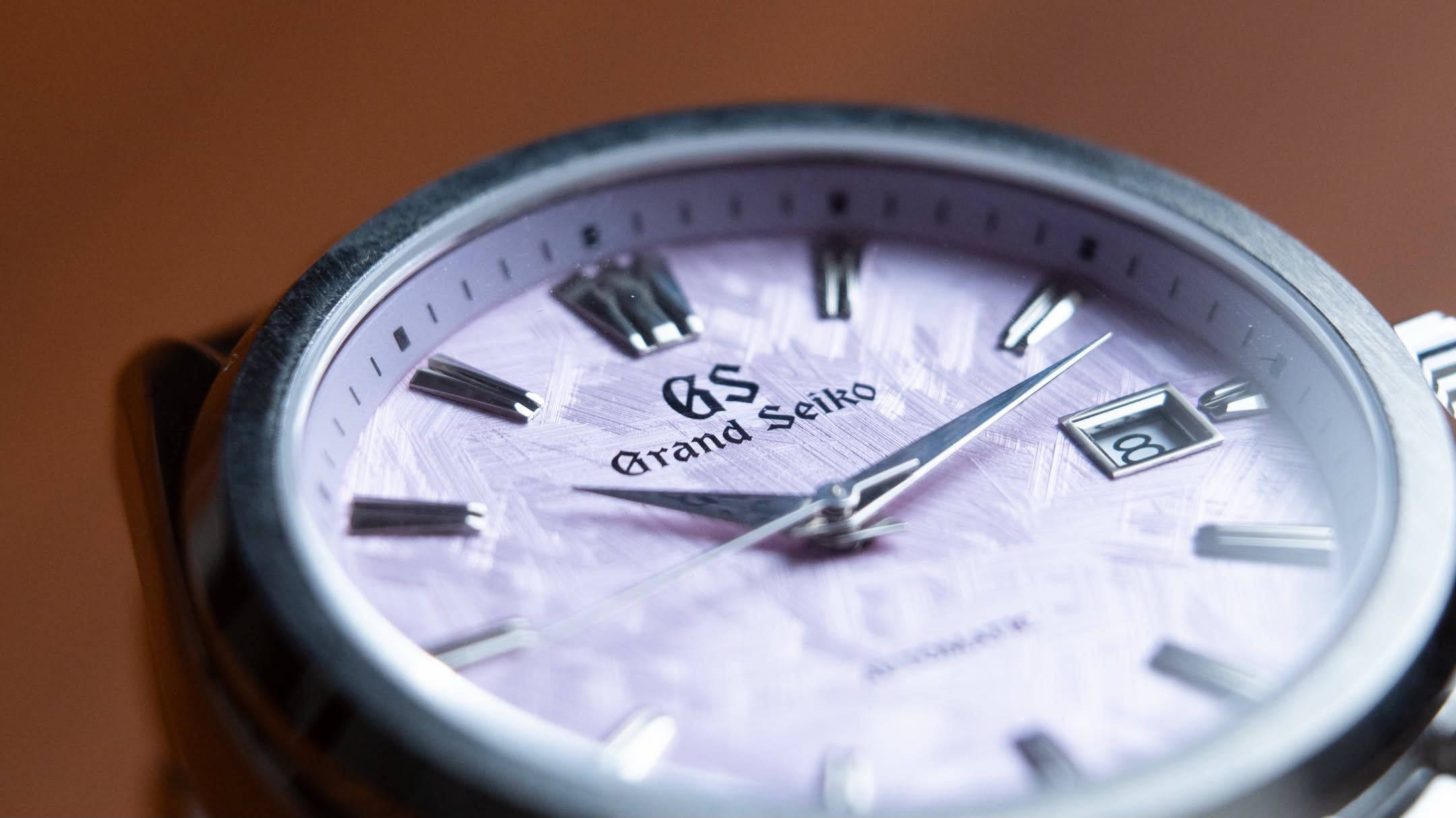 A close crop of the lilac dial, its frost-like texture and the date window at three.